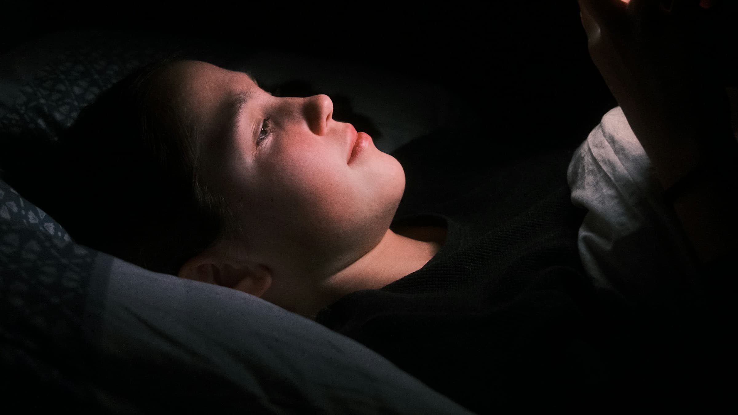 Ein Gesicht im Bett, nur vom Licht des Handys beleuchtet