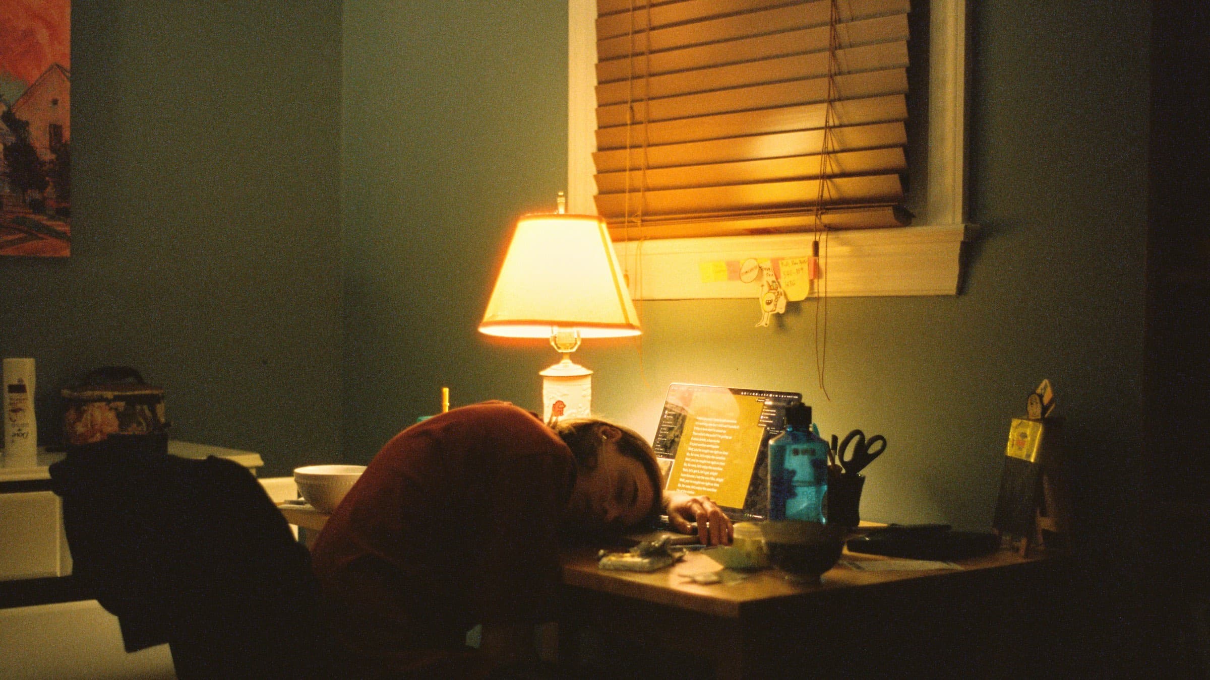 A person has fallen asleep at night under a desk lamp