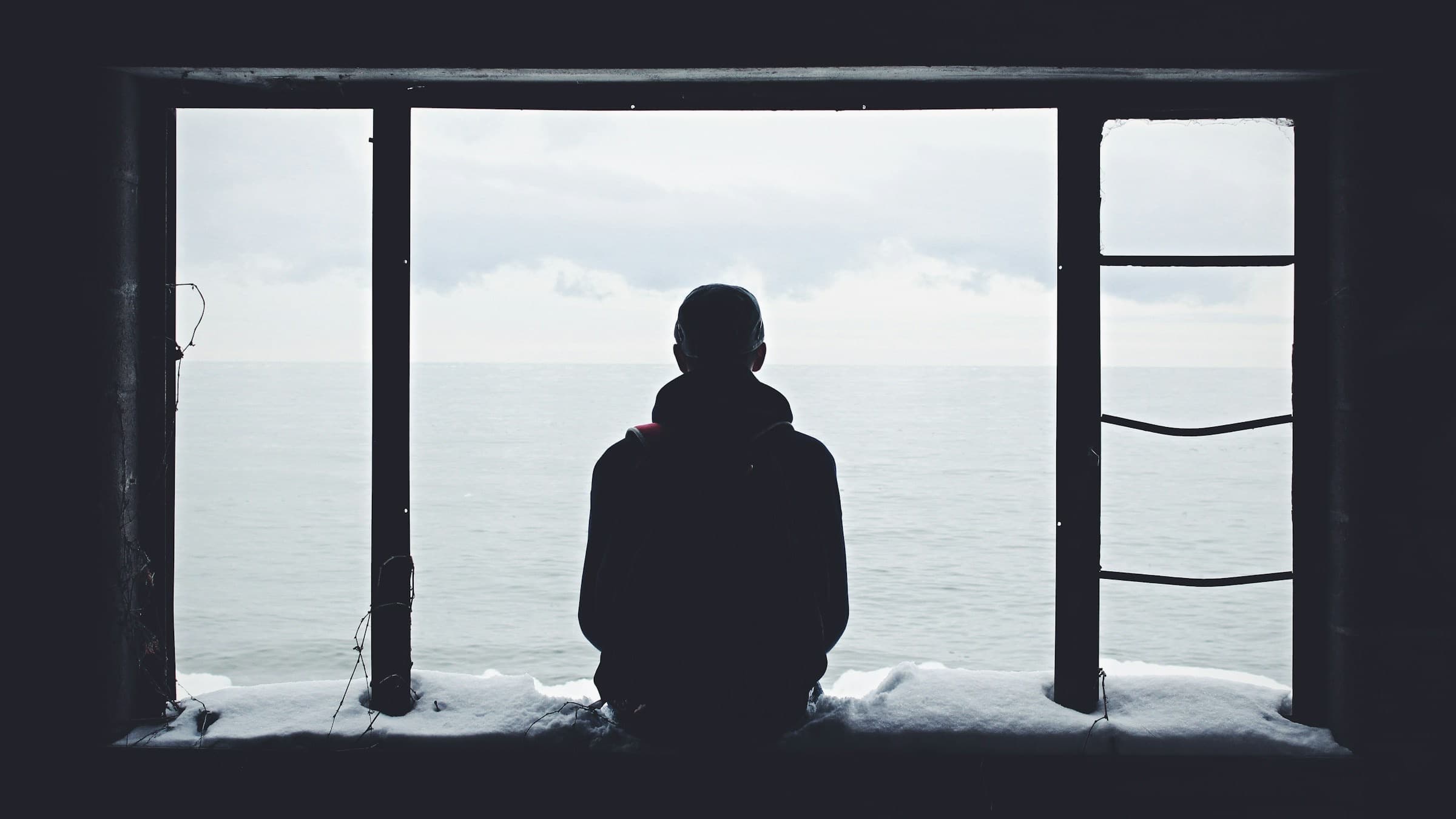 Silhouette of a person in a window frame, with the gray sea behind