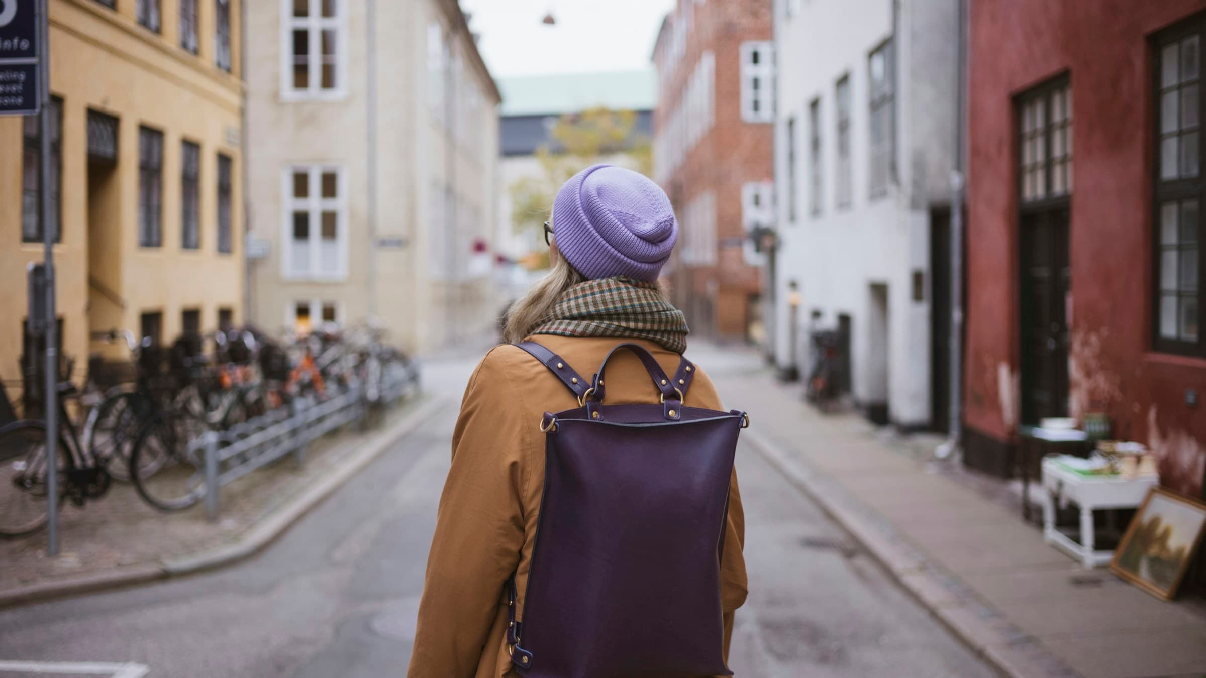 Student with a backpack seen from behind in an old-town alley lined with bicycles